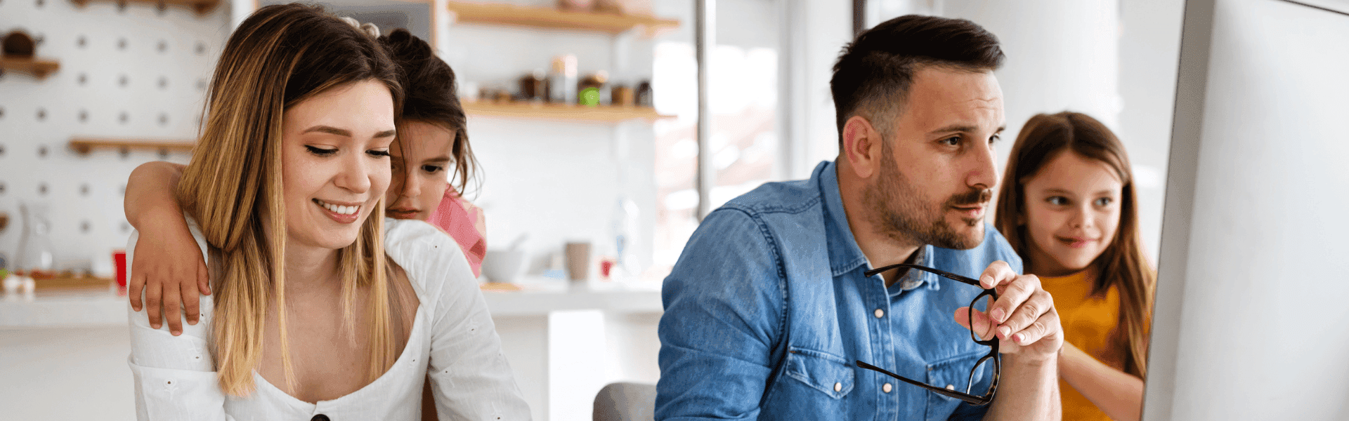 Eine Familie sitzt gemeinsam am Computer. Eine Frau und ein Mann arbeiten konzentriert, während zwei Kinder neugierig daneben stehen und zuschauen.
