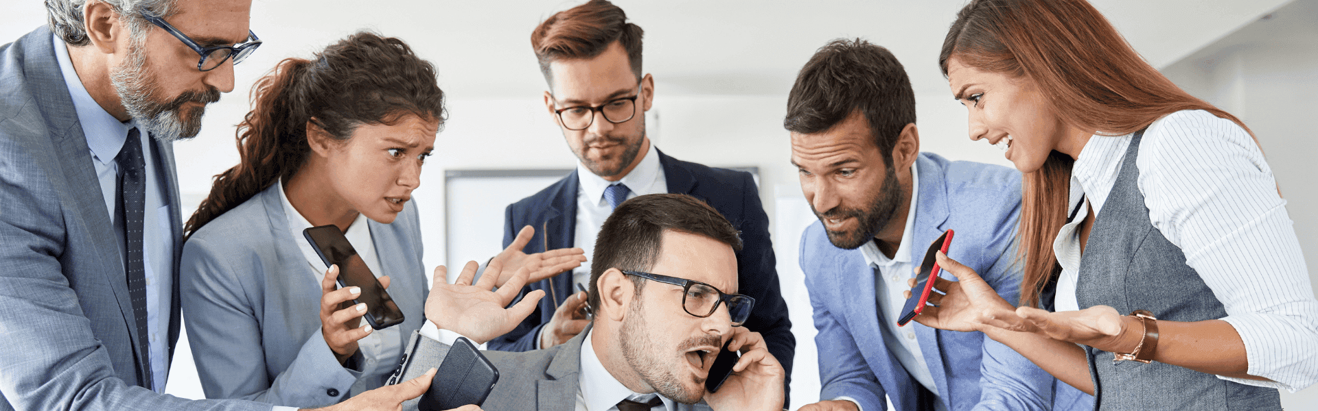 Mehrere Personen in Businesskleidung diskutieren lebhaft in einem Büro, zeigen auf Smartphones und gestikulieren, während eine Person im Mittelpunkt telefoniert und von allen Seiten angesprochen wird.
