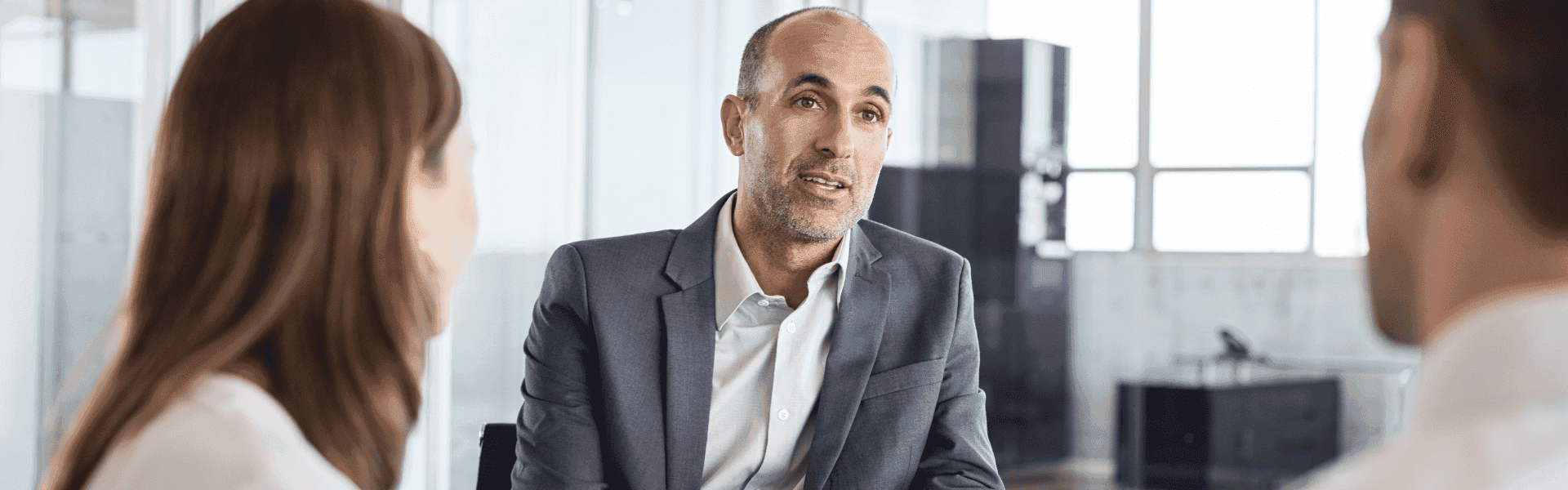 Drei Personen in einem Geschäftsgespräch in einem modernen Büro. Ein Mann spricht zu zwei anderen.